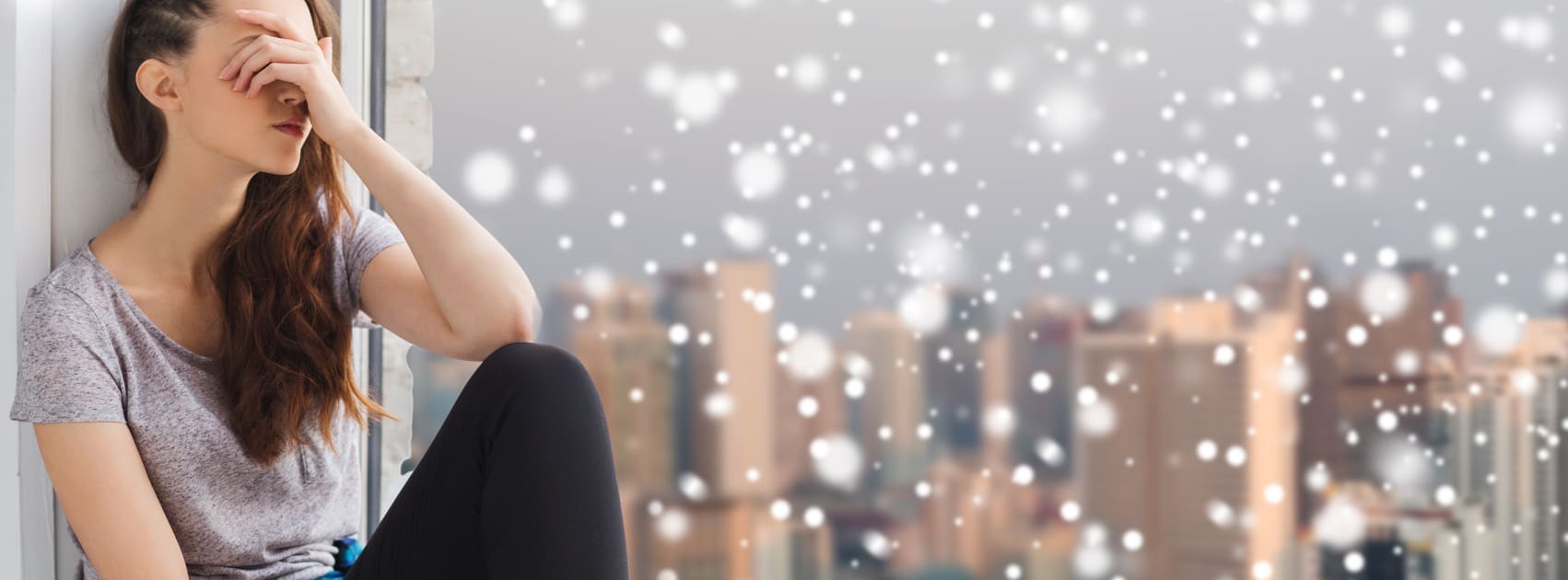 Adolescente mignonne triste et malheureuse assise sur la fenêtre sur le fond de la ville et de la neige